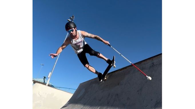 Justin Bishop skateboarding in a halfpipe with his white cane for guidance