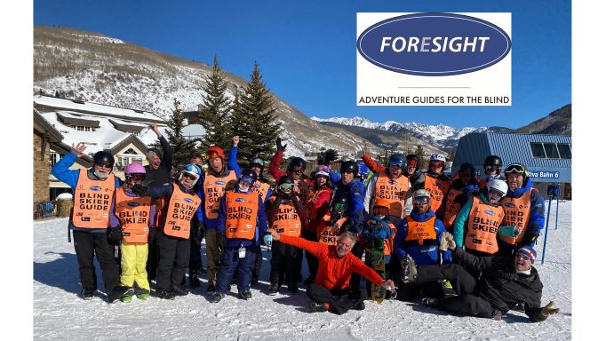 A group of blind skiers and sighted guides on Vail mountain with Foresight Adventure Guides for the Blind logo in upper corner