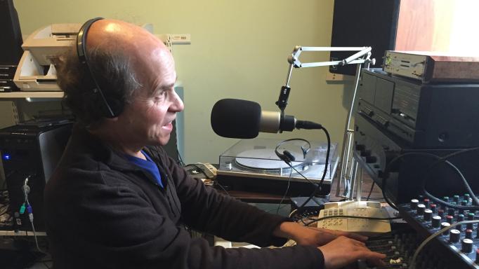 Photo of Glen Gordon in a recording studio. He is wearing headphones, speaking into a microphone, and working with a mixer.