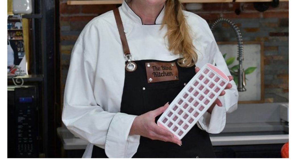 woman wearing a "the blind kitchen" apron holding an icecube tray to demonstrate using it to pre-measure ingredients
