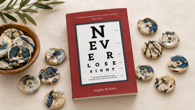 In the center of the image is the book 'Never Lose Sight' by Angela Ricketts. The title is printed to resemble an eye chart. Surrounding the book are a variety of sight stones, each of which is a combination of beige and medium blue. Everything is on a table covered by a lighter beige cloth.